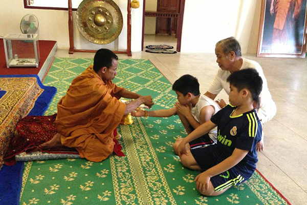 Inside Wat Phou Salao temple, the monk is cording the sew on the boy's hand for luck